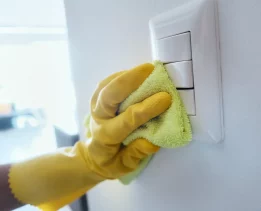 Close up view of person wiping electrical and light switches at home. People cleaning and disinfecting domestic surfaces to prevent virus and bacteria spread.